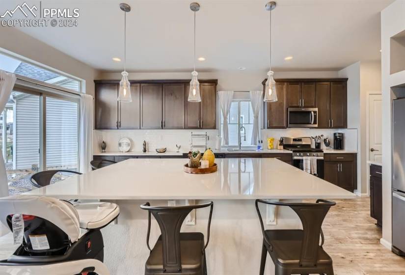 Kitchen featuring light hardwood / wood-style floors, a center island, tasteful backsplash, stainless steel appliances, and pendant lighting