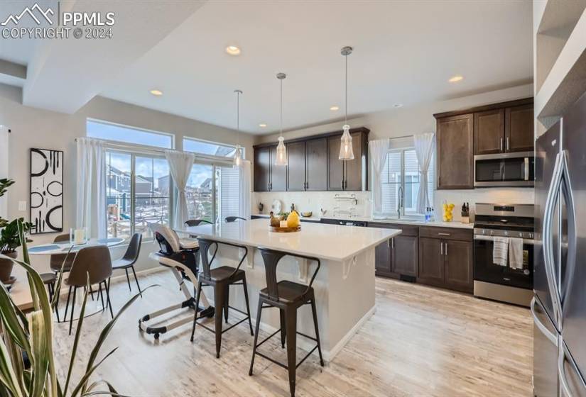 Kitchen with dark brown cabinets, stainless steel appliances, a kitchen island, light hardwood / wood-style floors, and decorative light fixtures
