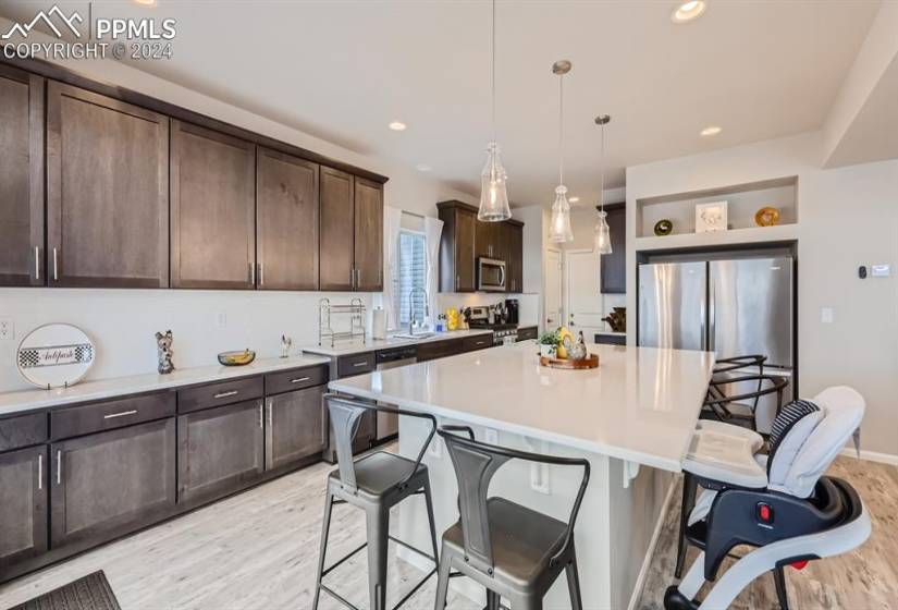 Kitchen with light wood-type flooring, a kitchen bar, a center island, pendant lighting, and appliances with stainless steel finishes