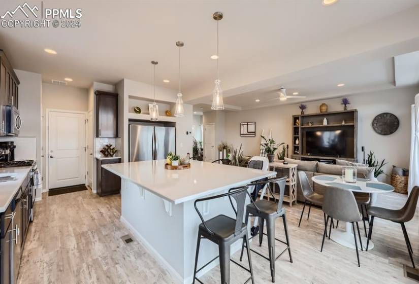 Kitchen with dark brown cabinetry, hanging light fixtures, appliances with stainless steel finishes, light hardwood / wood-style floors, and a center island