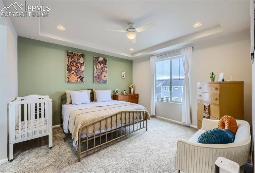 Bedroom with a raised ceiling, ceiling fan, and light colored carpet