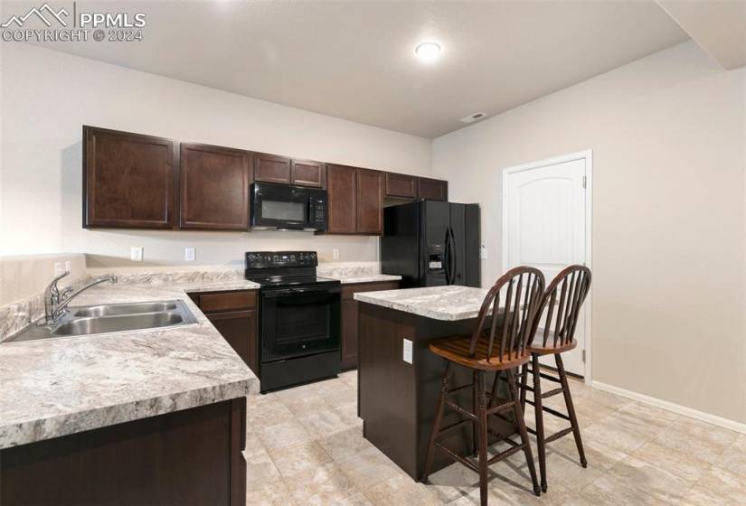 Kitchen with black appliances, a kitchen bar, dark brown cabinets, sink, and light tile flooring