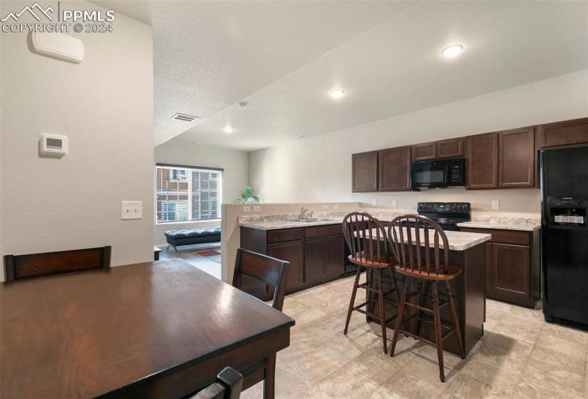 Kitchen with black appliances, a center island, a kitchen breakfast bar, dark brown cabinets, and light tile floors