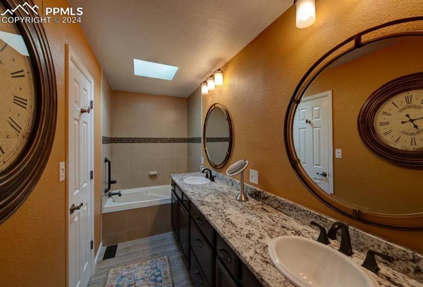 Primary bathroom with a textured ceiling, dual vanity, tiled bath, a skylight, and tile floors