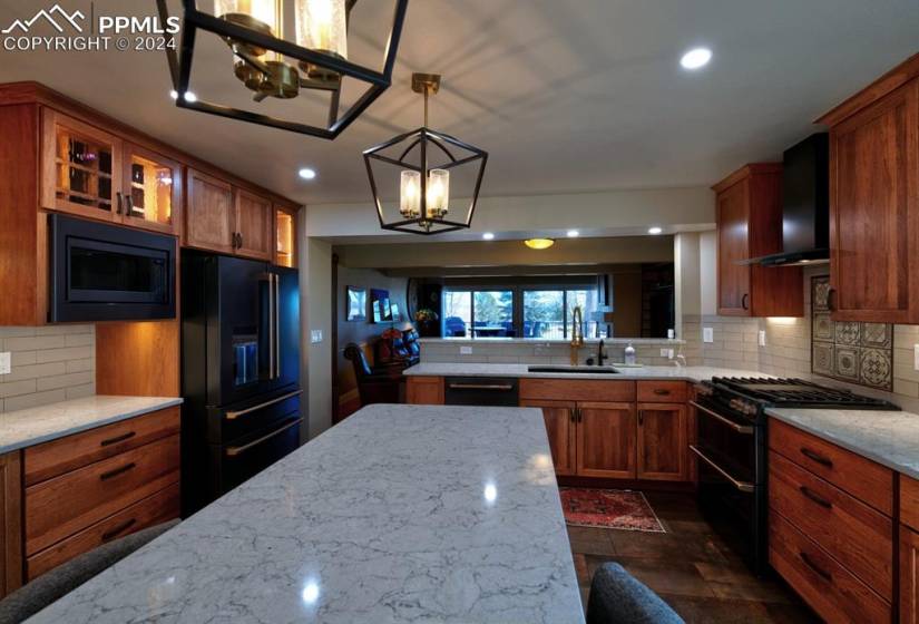 Kitchen featuring light stone counters, black appliances, tasteful backsplash, sink, and wall chimney range hood