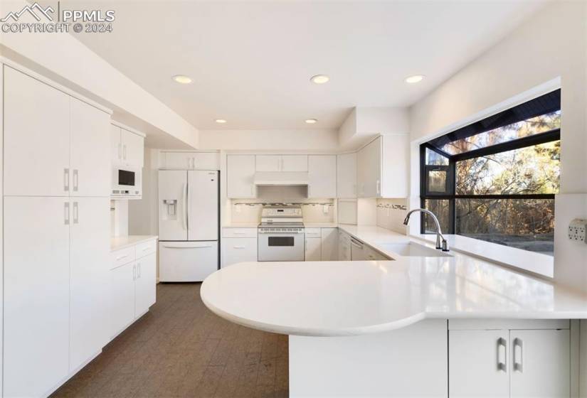 Kitchen featuring quartz countertops, backsplash, white cabinets, updated sink, and white appliances