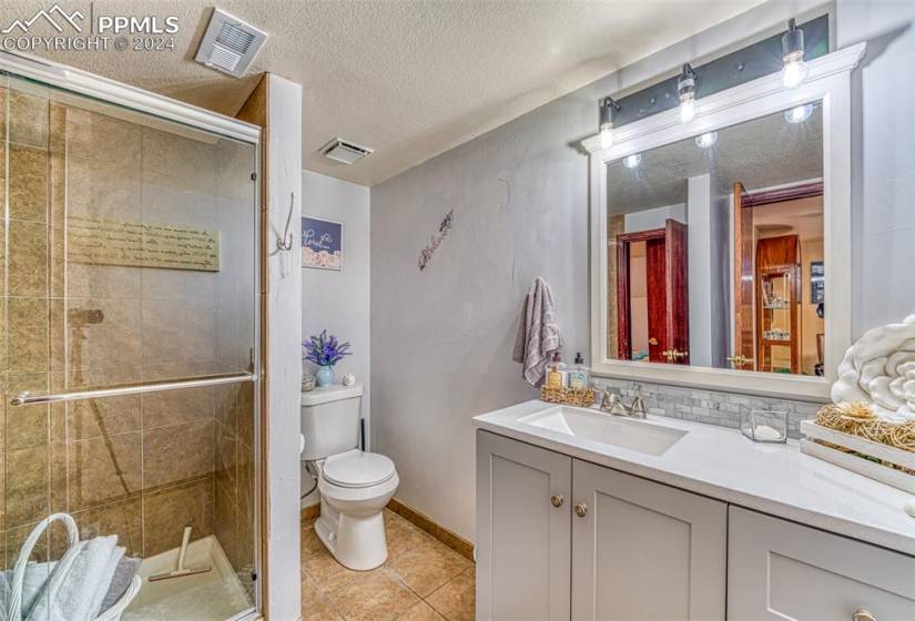 Bathroom with a textured ceiling, toilet, walk in shower, large vanity, and tile floors