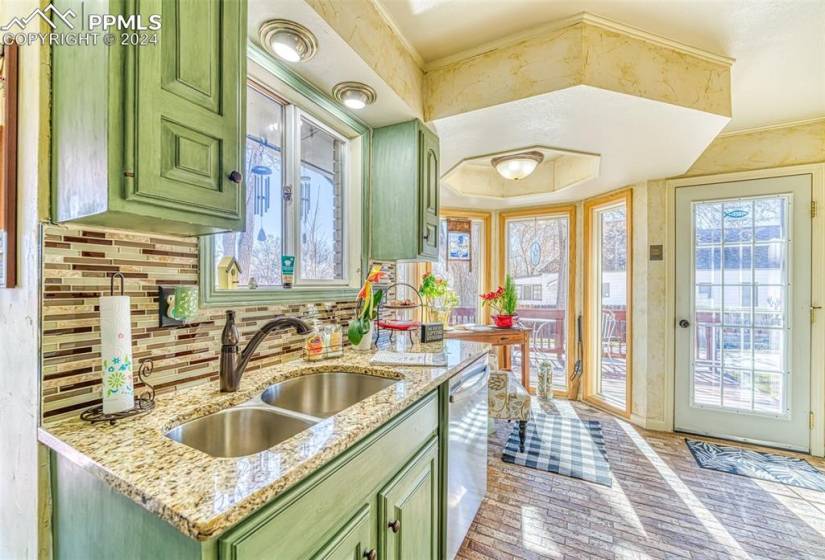 Kitchen featuring tasteful backsplash, a wealth of natural light, light stone countertops, and green cabinets