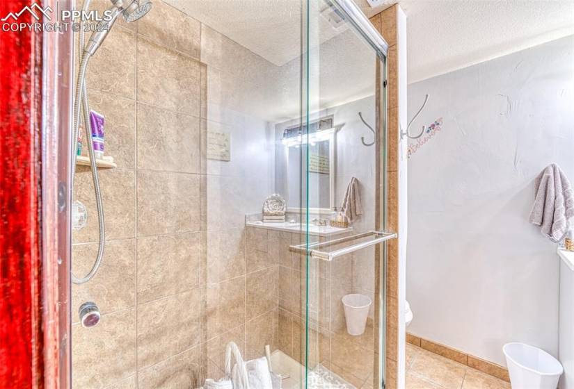Bathroom with a shower with door, a textured ceiling, and tile flooring