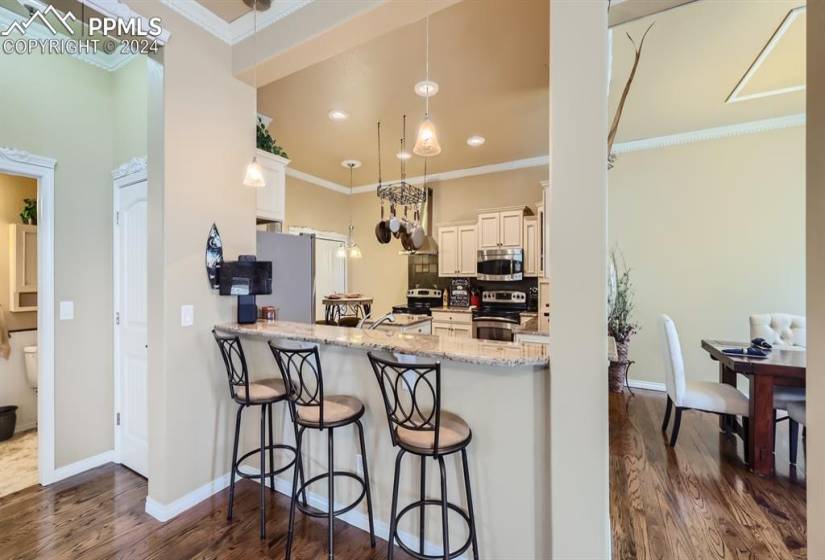 Kitchen featuring a kitchen breakfast bar, light stone countertops, dark hardwood / wood-style flooring, stainless steel appliances, and decorative light fixtures