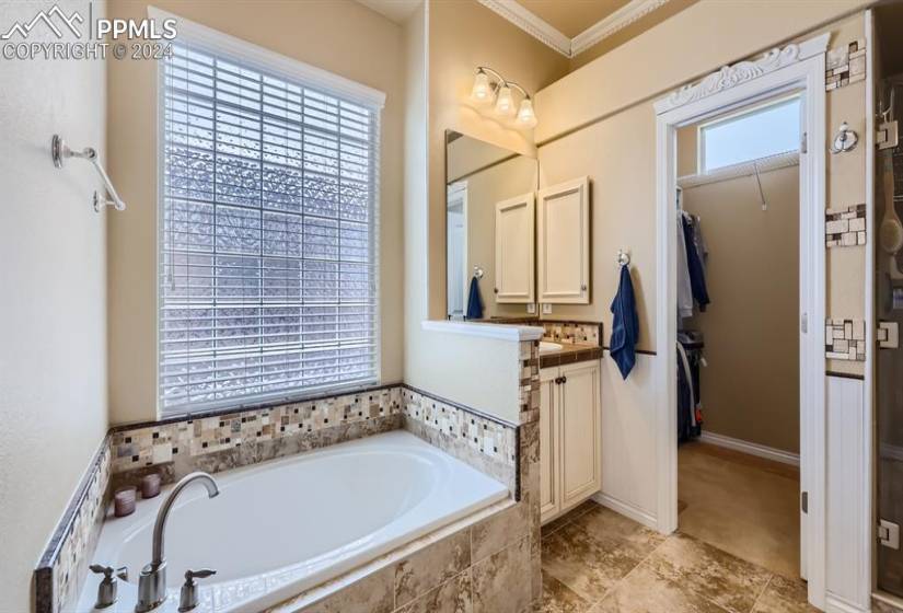 Bathroom featuring vanity, tiled tub, ornamental molding, and tile flooring