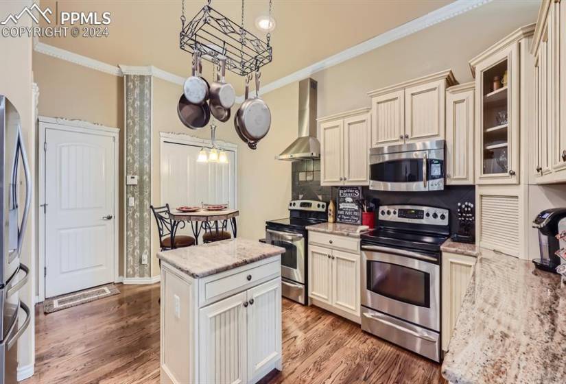 Kitchen featuring light wood-type flooring, appliances with stainless steel finishes, wall chimney range hood, and crown molding