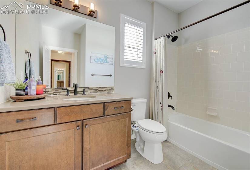 Full bathroom featuring shower / bath combo with shower curtain, backsplash, vanity, toilet, and tile flooring