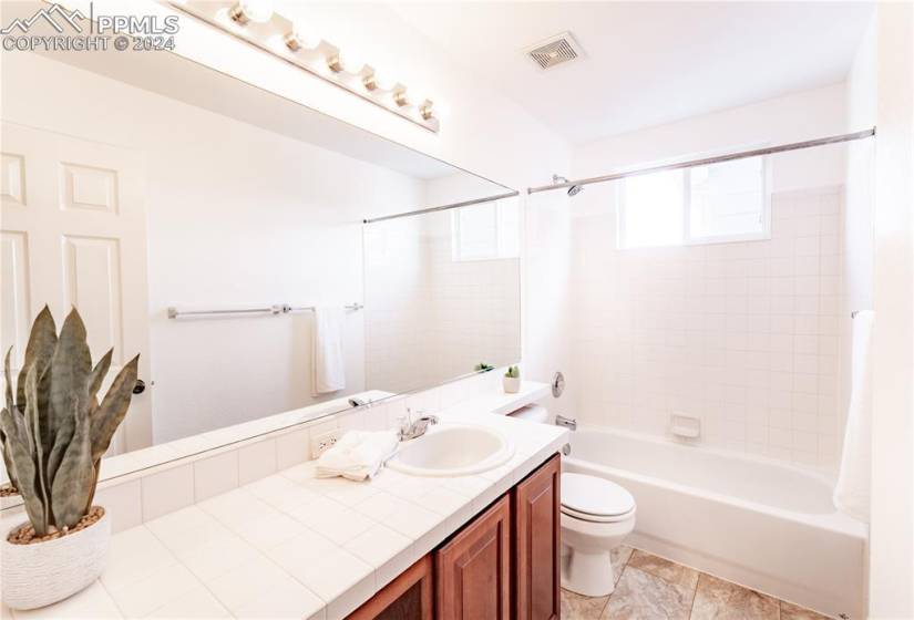 Full bathroom featuring tile floors, tiled shower / bath, vanity, and toilet