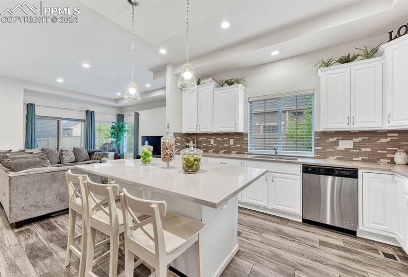 Kitchen with white cabinets, decorative light fixtures, backsplash, and stainless steel dishwasher