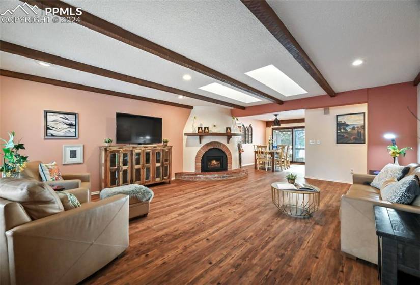Living room with exposed wood beams, skylights, dome fireplace, and wood flooring.