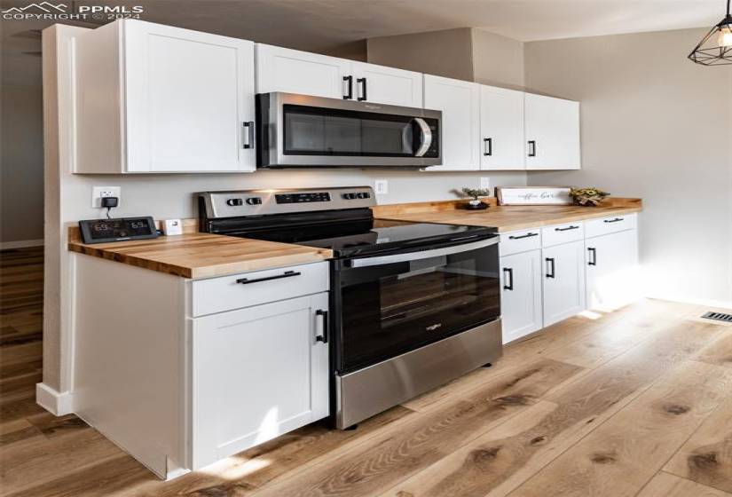 Kitchen with stainless steel appliances, white cabinets, light hardwood / wood-style flooring, wood counters, and vaulted ceiling