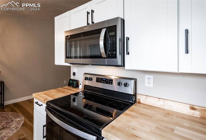 Kitchen with hardwood / wood-style floors, butcher block counters, stainless steel appliances, and white cabinetry