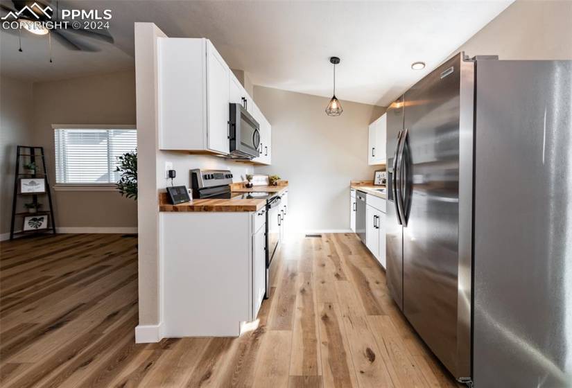 Kitchen with light wood-type flooring, white cabinets, wooden counters, pendant lighting, and appliances with stainless steel finishes