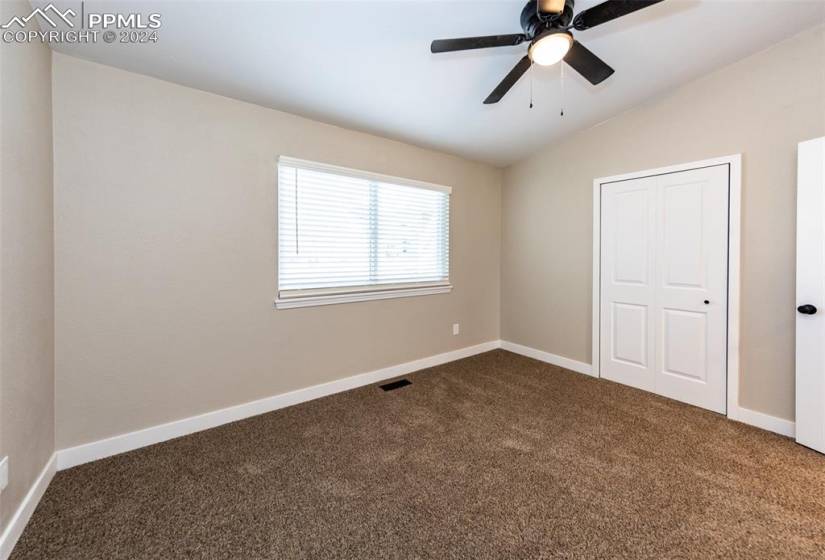 Unfurnished bedroom featuring dark carpet, vaulted ceiling, a closet, and ceiling fan