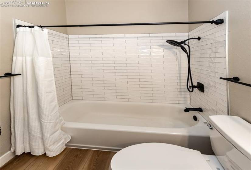 Bathroom featuring shower / tub combo with curtain, wood-type flooring, and toilet