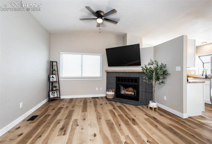 Unfurnished living room with lofted ceiling, ceiling fan, sink, light wood-type flooring, and a tiled fireplace