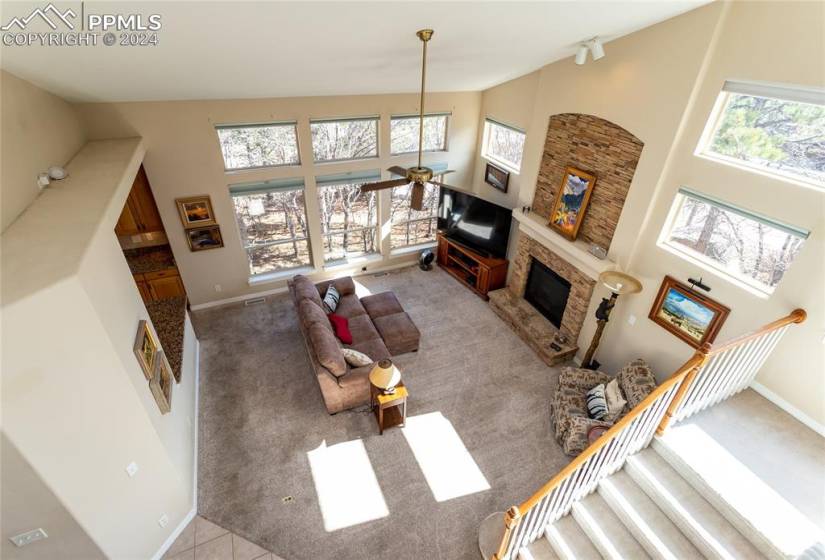 Living room with light colored carpet, high vaulted ceiling, plenty of natural light, and a stone fireplace