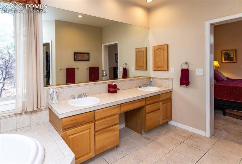 Bathroom with tile flooring, double sink, vanity with extensive cabinet space, and a bathing tub