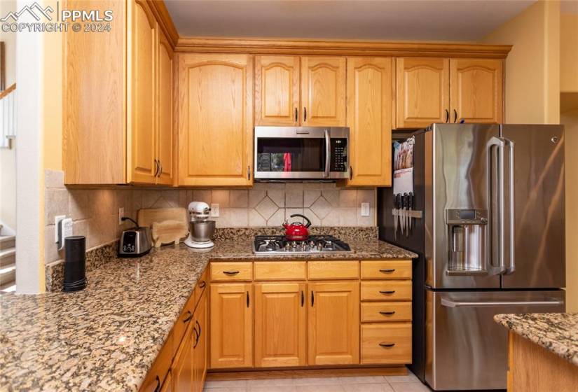 Kitchen with appliances with stainless steel finishes, tasteful backsplash, light tile floors, and light stone countertops