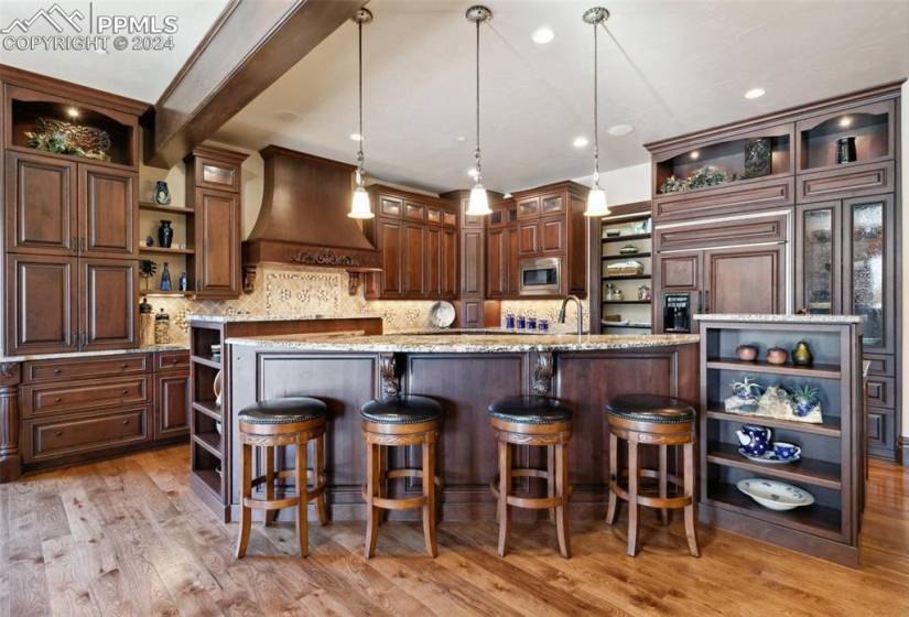 Kitchen featuring a kitchen bar, custom range hood, light hardwood / wood-style flooring, decorative light fixtures, and stainless steel microwave