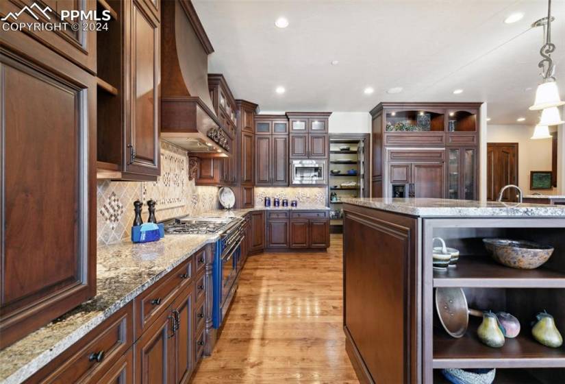 Kitchen featuring light wood-type flooring, tasteful backsplash, premium range hood, decorative light fixtures, and built in appliances