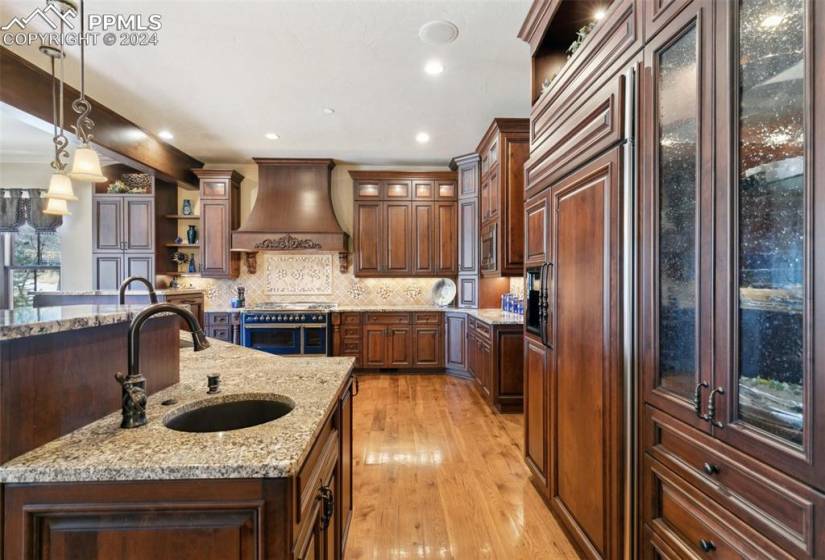 Kitchen with premium range hood, light stone counters, light hardwood / wood-style floors, sink, and decorative light fixtures