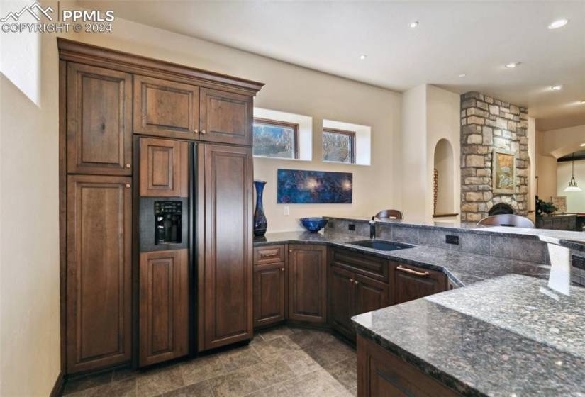 Kitchen with dark stone countertops, kitchen peninsula, tile flooring, sink, and paneled built in fridge