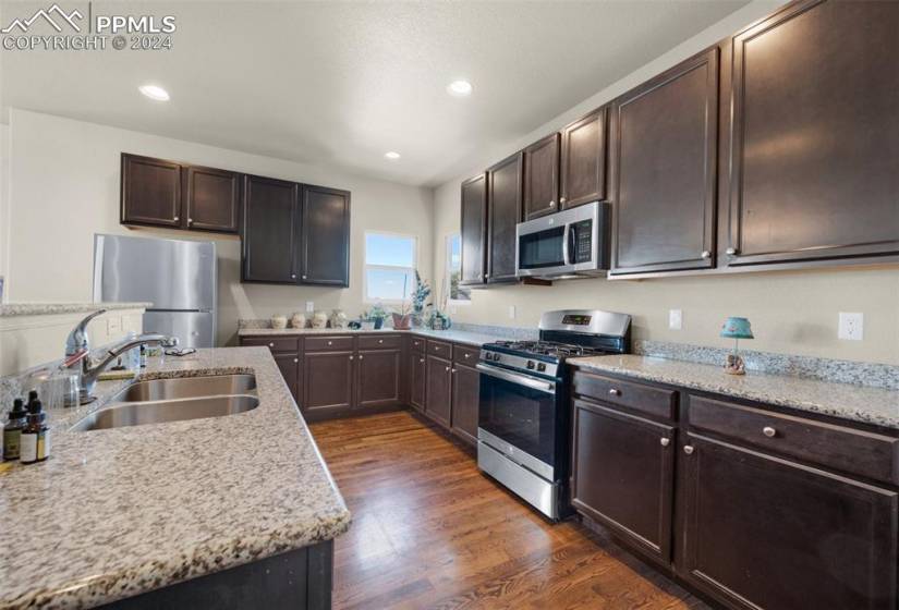 Kitchen with dark brown cabinets, light stone countertops, appliances with stainless steel finishes, sink, and dark hardwood / wood-style floors