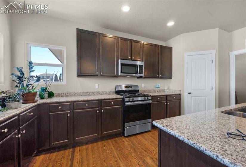 Kitchen with light stone countertops, appliances with stainless steel finishes, dark brown cabinets, and wood-type flooring