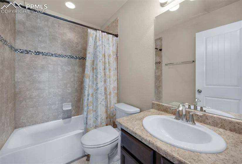 Full bathroom featuring large vanity, shower / bath combo with shower curtain, and toilet