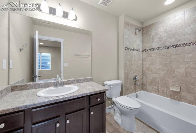 Full bathroom with toilet, tiled shower / bath combo, vanity with extensive cabinet space, and tile flooring