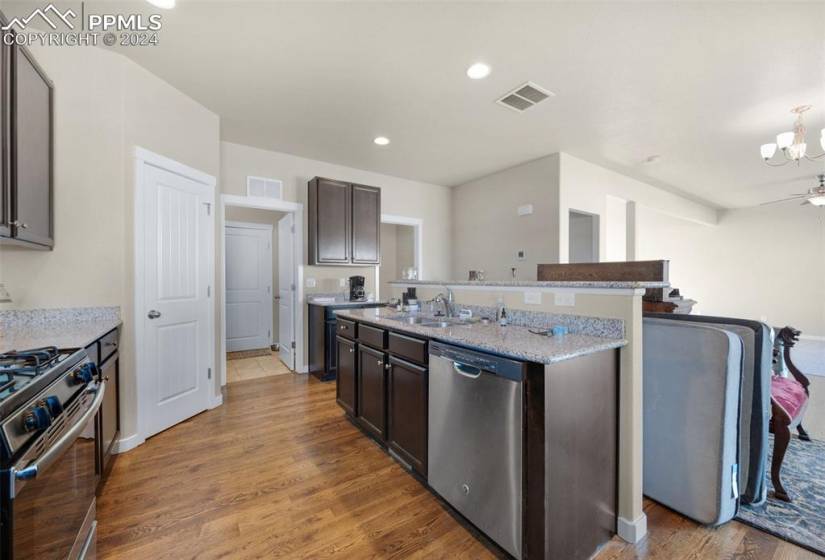 Kitchen featuring light wood-type flooring, appliances with stainless steel finishes, a center island with sink, and dark brown cabinetry