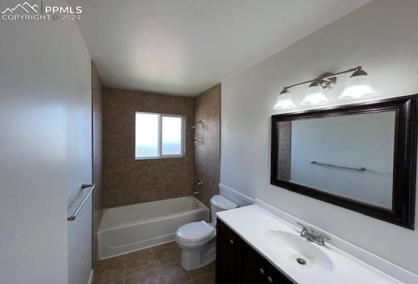 Full bathroom featuring a textured ceiling, vanity, tiled shower / bath combo, toilet, and tile flooring