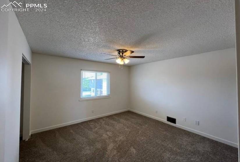 Spare room featuring dark colored carpet, ceiling fan, and a textured ceiling