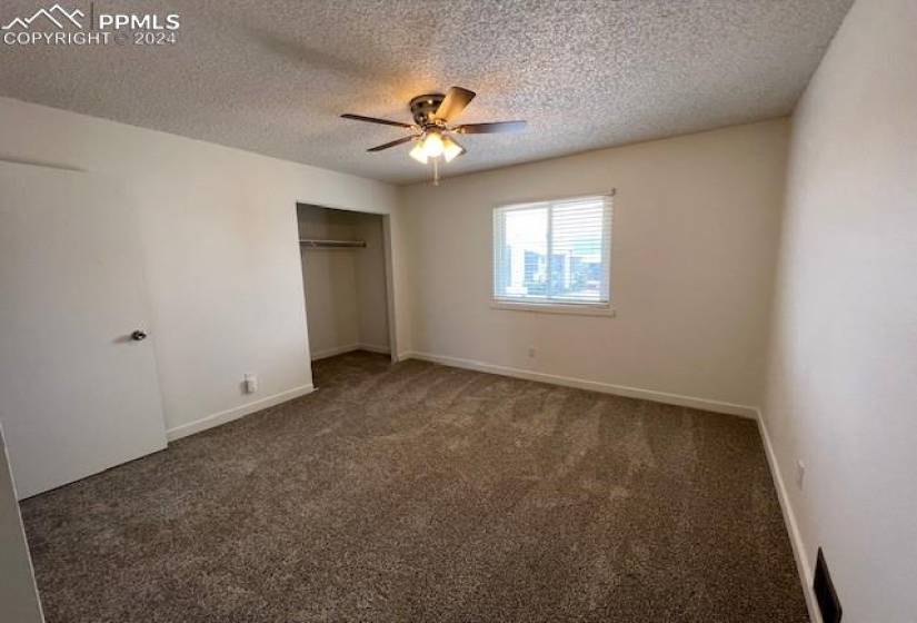 Unfurnished bedroom with a textured ceiling, ceiling fan, dark carpet, and a closet