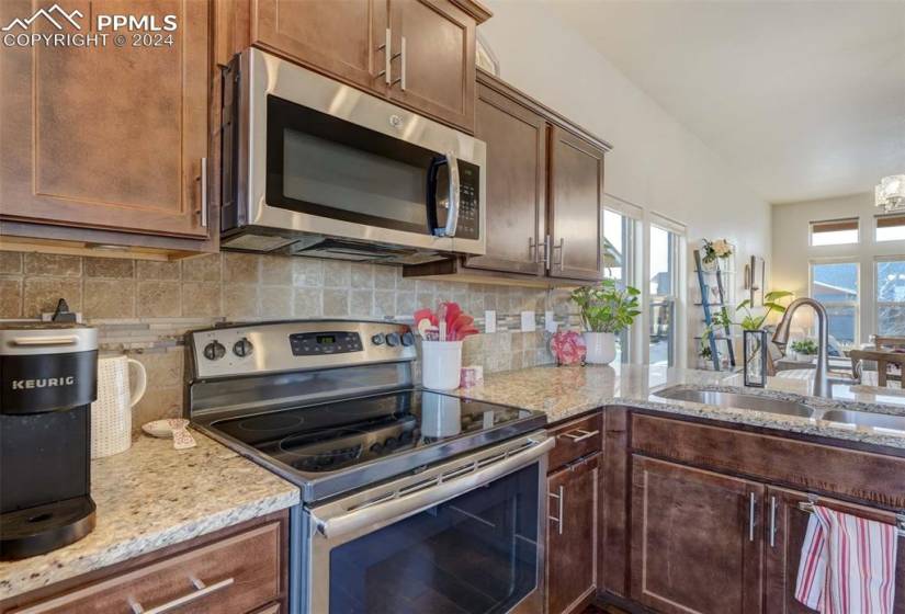 Kitchen featuring appliances with stainless steel finishes, light stone countertops, backsplash, and sink