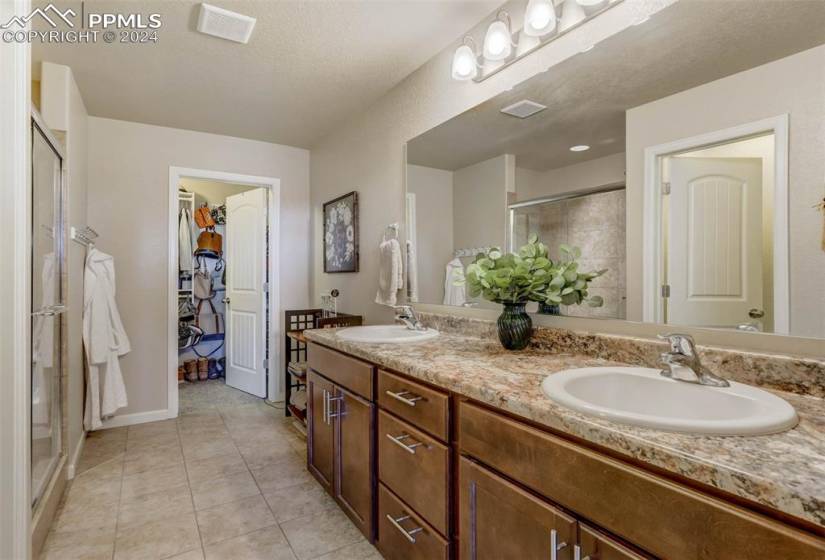 Bathroom with dual sinks, walk in shower, tile floors, and vanity with extensive cabinet space