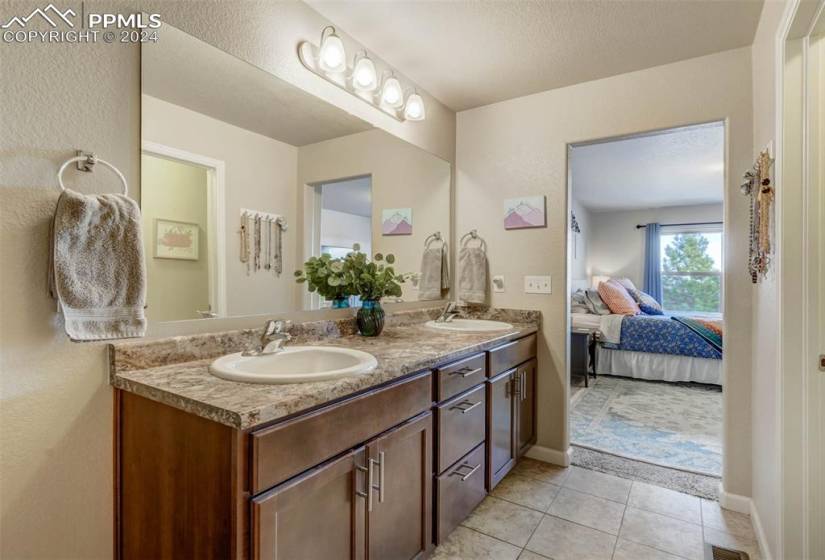 Bathroom featuring tile floors, double sink, vanity with extensive cabinet space, and a textured ceiling