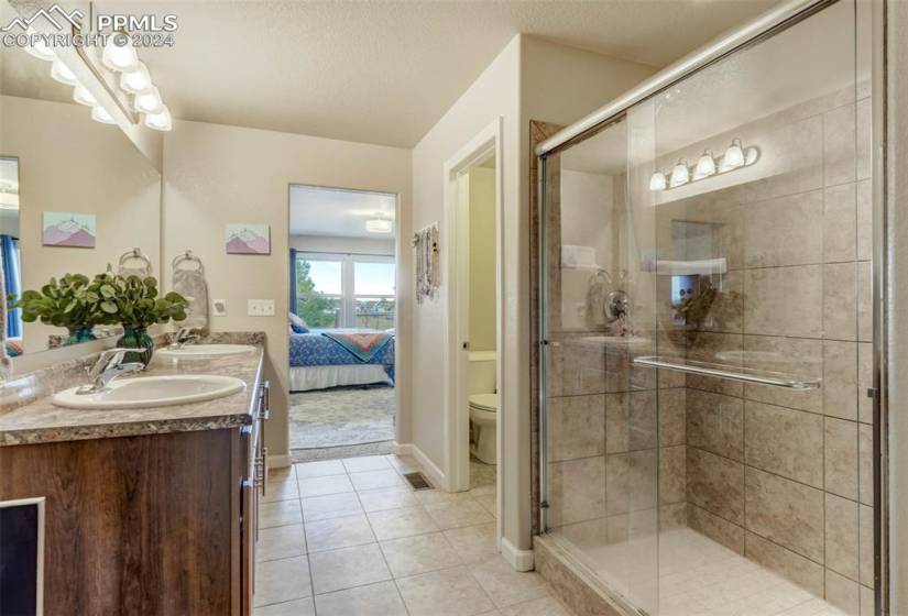 Bathroom featuring an enclosed shower, a textured ceiling, toilet, tile floors, and double sink vanity
