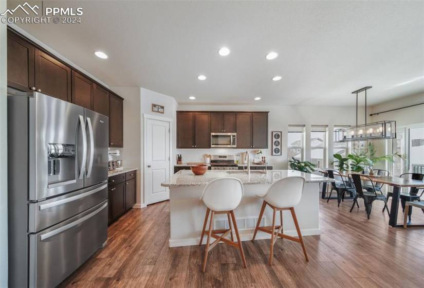 Kitchen with a center island with sink, light stone counters, hanging light fixtures, dark LVP floors, and appliances with stainless steel finishes