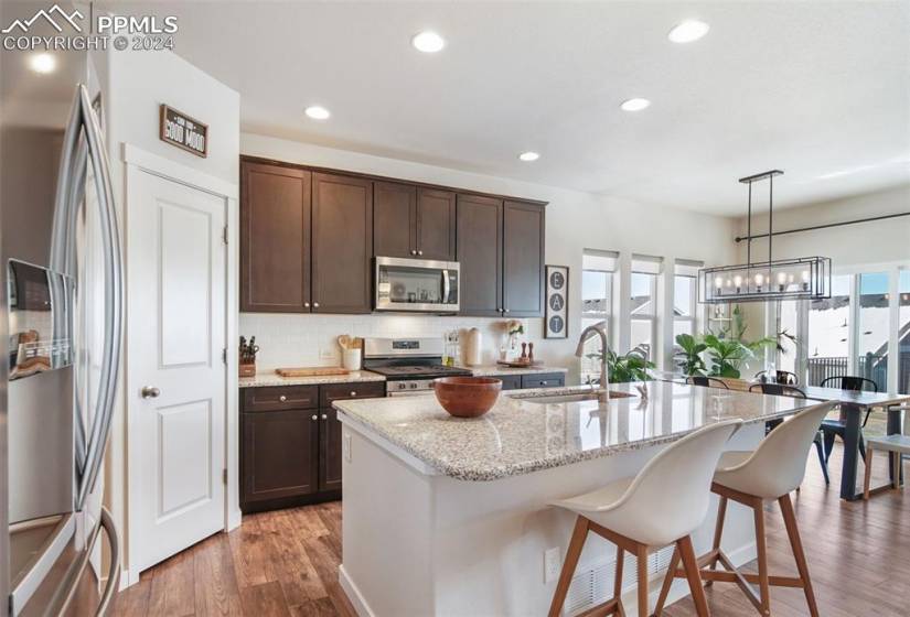 Kitchen featuring pendant lighting, hardwood / wood-style floors, light stone countertops, a center island with sink, and appliances with stainless steel finishes