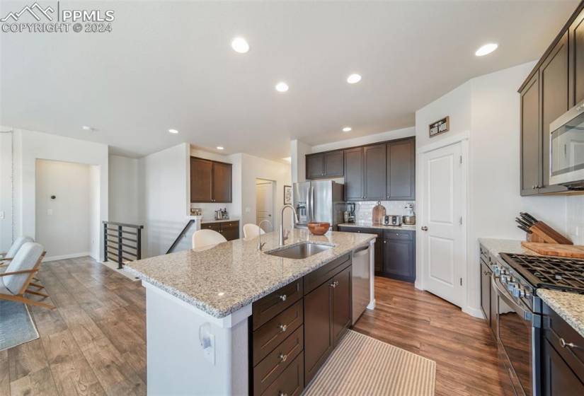 Kitchen with a center island with sink, light stone countertops, dark LVP flooring, sink, and stainless steel appliances