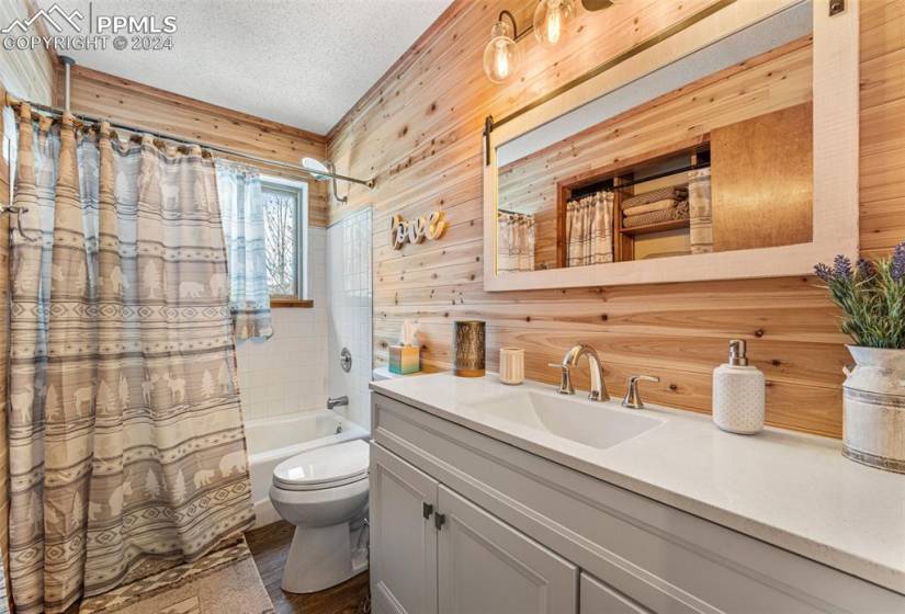Full bathroom with a textured ceiling, wooden walls, toilet, oversized vanity, and shower / tub combo with curtain