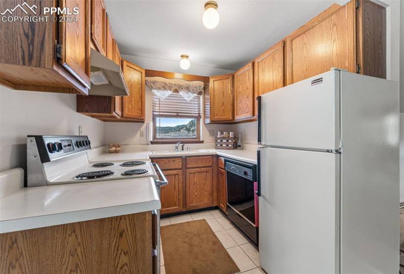 Kitchen featuring light tile flooring, black dishwasher, white fridge, stove, and wall chimney exhaust hood